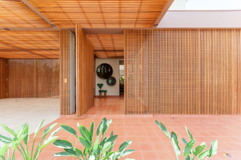 Na entrada dessa residência projetada pela dupla do escritório Paiva e Passarini Arquitetura, o pergolado foi estendido com o intuito de propiciar as diversas oportunidades de luz natural ao longo do dia. A entrada e a fachada da residência revelam um destaque amadeirado encantador!